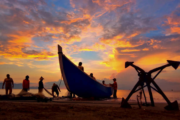 Fishermen Banda Aceh are repairing their fishing nets on the beach at sunset. In the reddish-orange glow of twilight, they diligently clean the nets from the day's catch. A peaceful atmosphere is created amidst the shimmering sea, while the sky welcomes the night with captivating warmth. Banda Aceh-Indonesia 04/03/2019