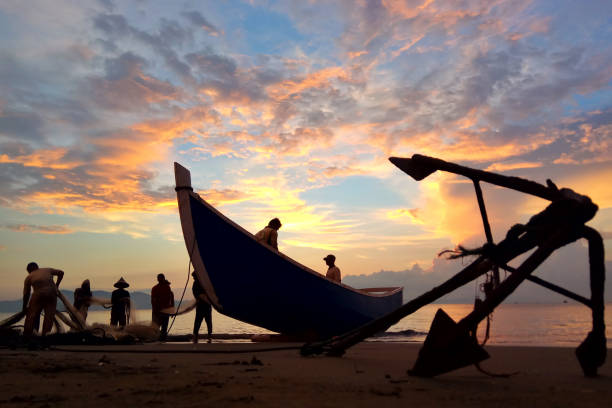 Fishermen Banda Aceh are repairing their fishing nets on the beach at sunset. In the reddish-orange glow of twilight, they diligently clean the nets from the day's catch. A peaceful atmosphere is created amidst the shimmering sea, while the sky welcomes the night with captivating warmth. Banda Aceh-Indonesia 04/03/2019