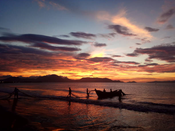 Fishermen Banda Aceh are repairing their fishing nets on the beach at sunset. In the reddish-orange glow of twilight, they diligently clean the nets from the day's catch. A peaceful atmosphere is created amidst the shimmering sea, while the sky welcomes the night with captivating warmth. Banda Aceh-Indonesia 04/03/2019