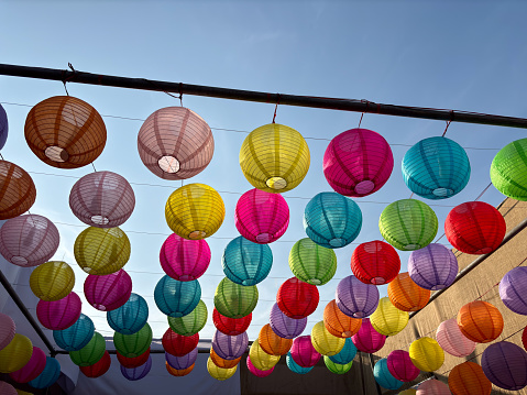 Colourful lanterns hanging above street during multicultural festival. Multiple Objects.