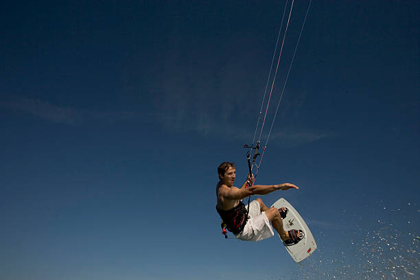 masculino kiteboarder ar, braços esticados, vista de ângulo baixo - skill side view jumping mid air - fotografias e filmes do acervo