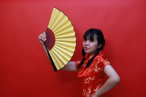 Happy Asian young girl wearing a traditional cheongsam qipao dress isolated on a red background. Happy Chinese New Year Women with Happy Expression Concept