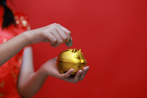 A cute Young Asian girl dressed in traditional cheongsam holds a gold piggy bank on Chinese New Year's Day