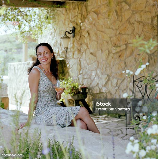 Frau Sitzt Auf Stein Wand Und Hältst Wein Glas Stockfoto und mehr Bilder von 35-39 Jahre - 35-39 Jahre, Baumblüte, Blick in die Kamera