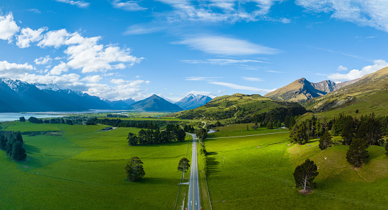 Experience breathtaking vistas from above at Glenorchy, New Zealand, where mountains dominate the stunning landscape. In front a straight road through green fields.