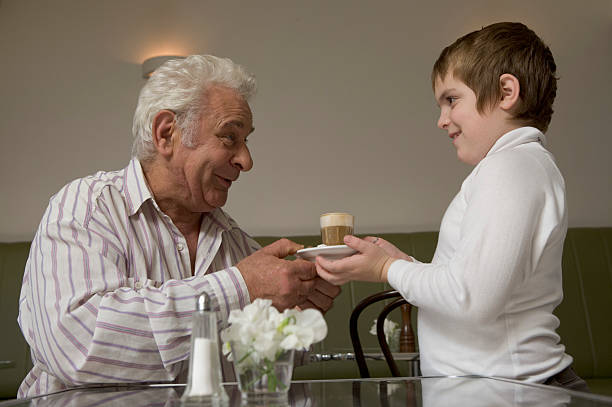 Boy (8-10) handing drink to grandfather, side view stock photo