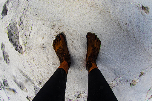 Looking at a mans feet covered in black dirt standing on white sand