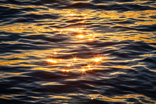 Brilliant gold lens flare on textured ripples on ocean surface reflecting the sunrise. Photographed in Western Australia.