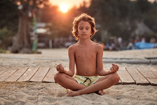 Mindfulness, beautiful boy doing yoga and breathing exercises at sunset on the beach.