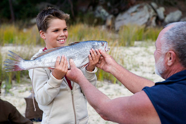 Boy (9-11) showing father fish, smiling, outdoors stock photo