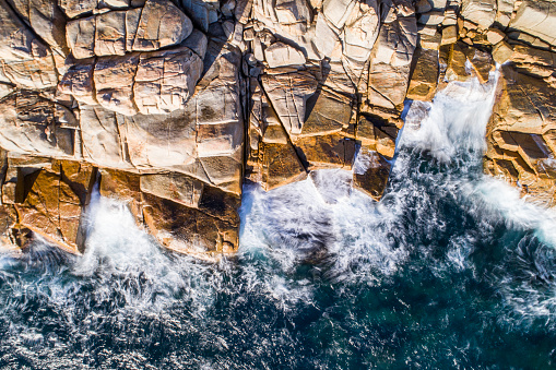 Aerial view of coastal scene with bay of water and waves crashing against rocks at sunrise. Photographed in Esperance, Western Australia.