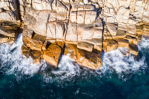 Aerial view of coastal scene with bay of water and waves crashing against rocks at sunrise. Photographed in Esperance, Western Australia.