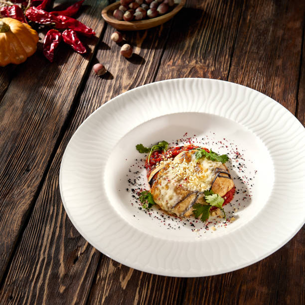Baked eggplant roll with cheese and tomatoes, elegantly plated on a white dish.