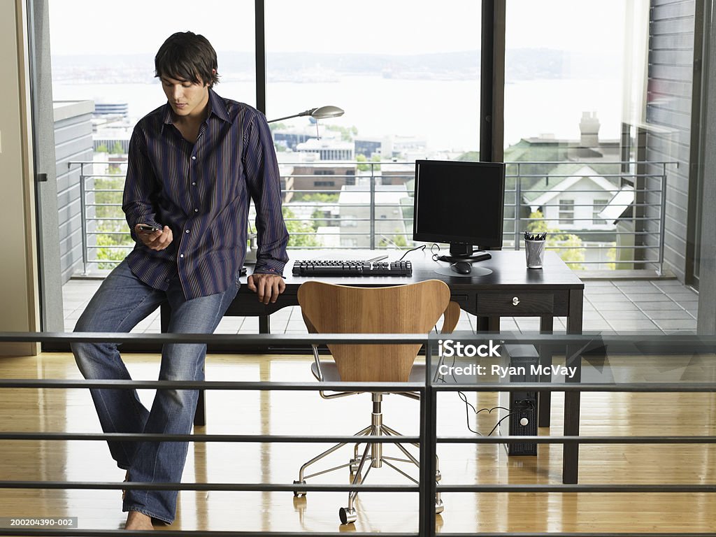 Homem Jovem Sentado na beirada da mesa, segurando palmtop - Foto de stock de Camisa royalty-free