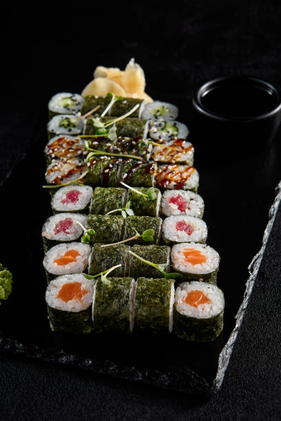 istock Assorted hosomaki sushi set with salmon, tuna, eel, and cucumber on black textured background 2002043987