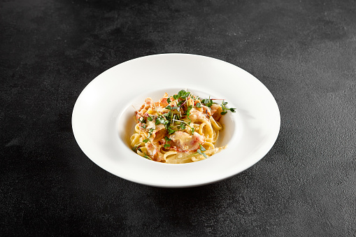 Classic carbonara pasta with a creamy sauce and garnished with fresh herbs, presented on a white plate.