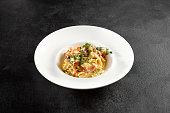 Classic carbonara pasta with a creamy sauce and garnished with fresh herbs, presented on a white plate