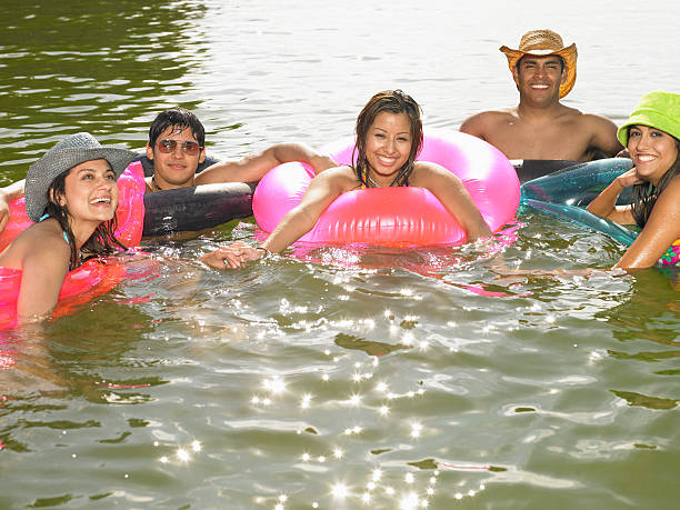 cinco jovens adultos em boias no lago, sorrindo - inner tube swimming lake water - fotografias e filmes do acervo