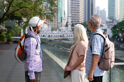 Two Asian senior tourist enjoy the city tour and listening to a local tour guide explaining about the architecture and the history of the River of Life in the city of Kuala Lumpur.