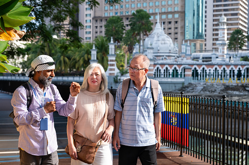 A mature Sikh tour guide leading two senior Asian traveler through the famous landmarks in the city of Kuala Lumpur, Malaysia.