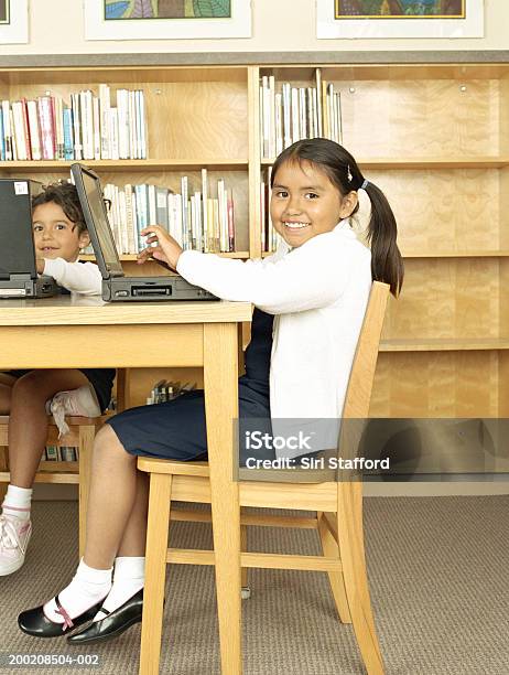 Photo libre de droit de Filles Assis À Table Dans La Bibliothèque À Laide Dun Ordinateur Portable Portrait banque d'images et plus d'images libres de droit de 6-7 ans