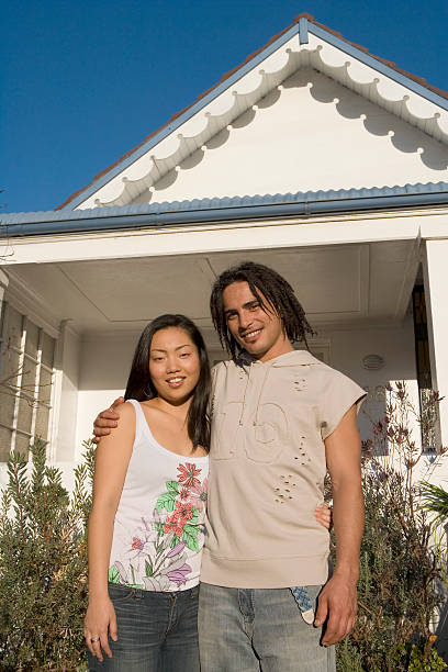 Young couple outside house, man's arm around woman, portrait stock photo