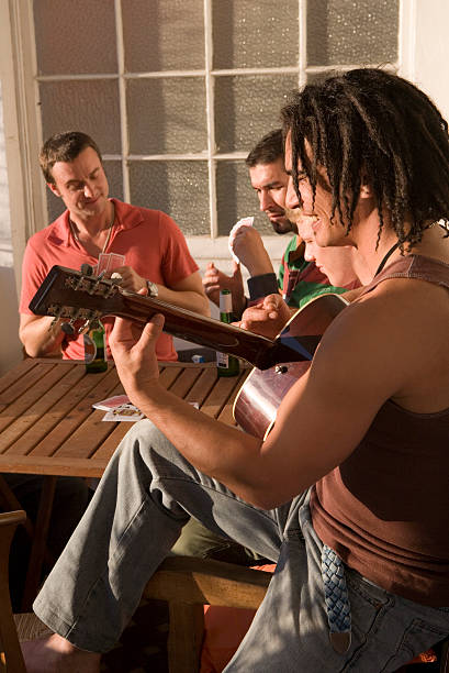 Group of men relaxing on veranda playing cards, one man playing guitar stock photo