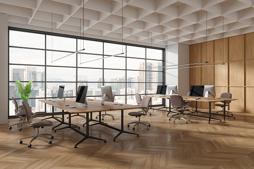 Corner view of coworking interior with chairs and pc desktop, table in row on hardwood floor. Office business workplace and panoramic window on Kuala Lumpur skyscrapers. 3D rendering