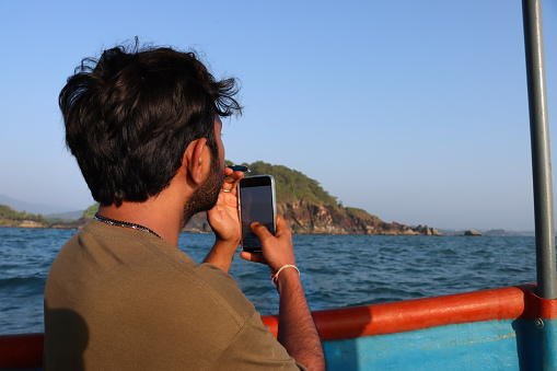Stock photo showing close-up, rear view of unrecognisable male tourist travelling on calm sea on a dolphin spotting pleasure tour boat at sunset.