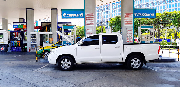 Bangkok, Thailand - December 23, 2023: White pickup car or truck opening hood for filling NGV or Natural Gas for Vehicle gas at gas station. Need Energy, Transportation and Power for driving concept.