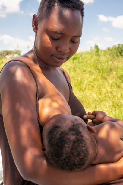 A young  mother breastfeeding fer baby outdoors under a tree shade