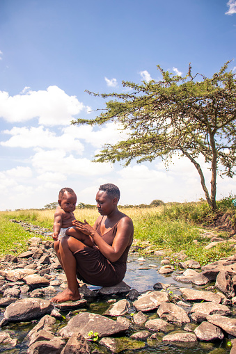 A young  african mother and her baby sitting  on a rocky riverbed