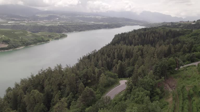 Drone shot flying over Lago di Santa Giustina near Trentino in Italy on a cloudy day with mountains and water surrounded by green fields and trees LOG