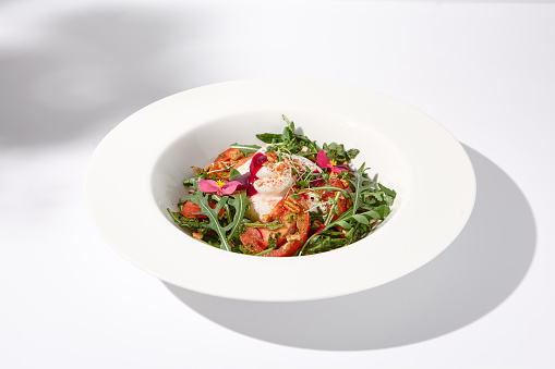 Italian salad with burrata, tomatoes, and arugula in shadow, garnished with edible flowers.