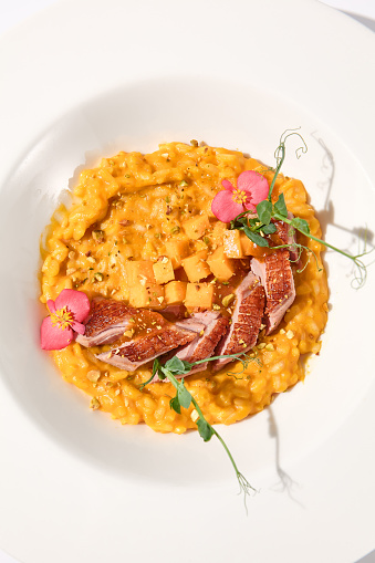 Top view of duck breast with pumpkin risotto on white, ideal for autumn menu promotions and food blogging.