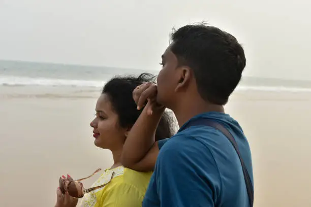 Just-married Indian couple standing by blue lagoon and enjoying each others company on their honeymoon holiday.