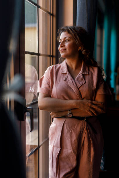 istock Charming woman standing by the window, smiling and contemplating 2002208463
