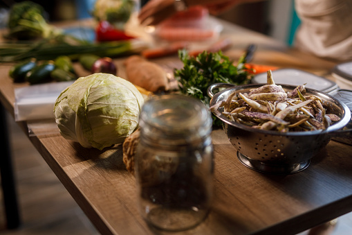 Cut out shot of diligent homemaker, wearing an apron, standing over a kitchen table, chopping and preparing various colorful vegetables for winter preservation.