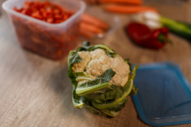 Cut out shot of diligent homemaker, wearing an apron, standing over a kitchen table, chopping and preparing various colorful vegetables for winter preservation.
