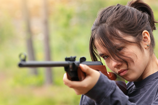 Teenage girl taking aim on a target with an air rifle.