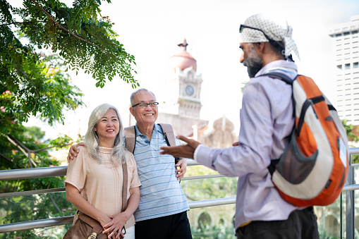 Senior Sikh tour guide explaining the history of the heritage Sultan Abdul Samad Buildings to two senior Asian traveler at the Merdeka Square, Kuala Lumpur.