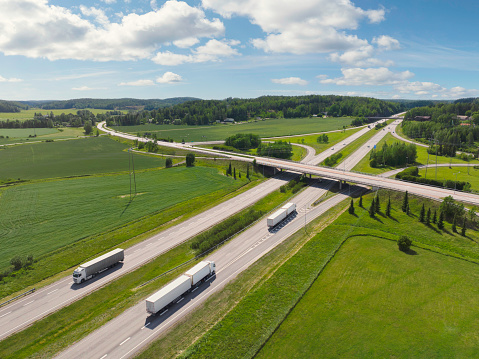 Aerial view of trucks on a highway through a countryside landscape in summer - highway E18 between Turku and Helsinki, Finland.