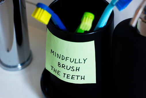 Close-up of a cup for toothbrushes with a sticker containing a handwritten inscription: Mindfully brush the teeth. Mindfulness training concept