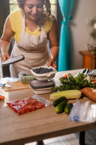 Close up shot of unrecognizable homemaker standing over a kitchen table and preserving fresh blueberries in a reusable container, for the winter.