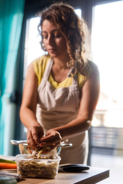 Candid shot of diligent homemaker standing over kitchen table, chopping and preserving various vegetables for the winter.
