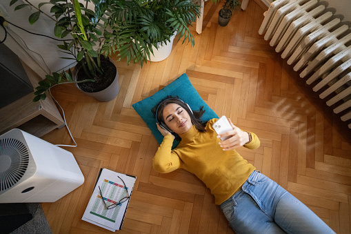 High angle view of young woman relaxing while lying on floor and listening music on wireless headphones while taking break from learning at home