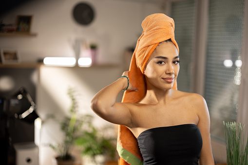 Beautiful young woman with towel on her head standing and looking at camera at home