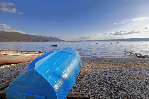 Vernacular rowboats stranded on the pebble Saraiste beach along Kosta Abrash street facing the east-south-west lakeshore, the snowcapped Galicica mountain on the left-east bank. Ohrid-North Macedonia.