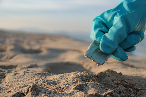 close-up of a hand picking up plastics on the beach