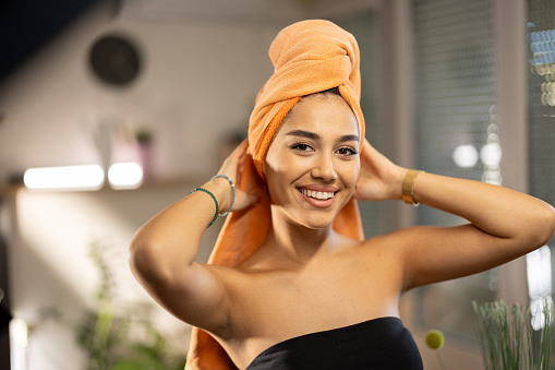 Beautiful young woman with towel on her head standing and looking at camera at home